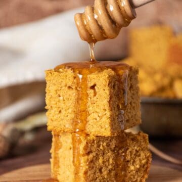 2 slices of cornbread stacked on one another, with honey being drizzled over them.