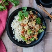 Stir fry on a plate, over brown rice, garnished with sesame seeds and cilantro.