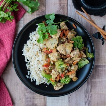 Stir fry on a plate, over brown rice, garnished with sesame seeds and cilantro.