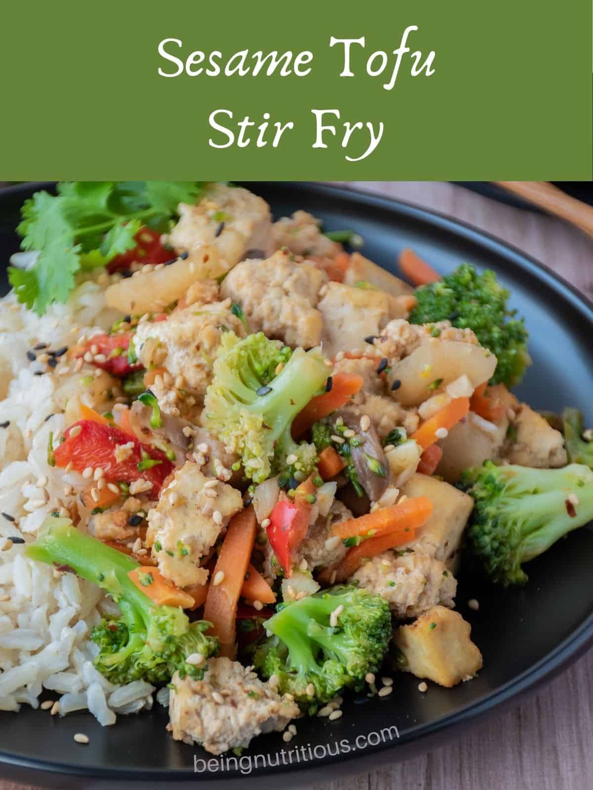 Stir fry on a plate, over brown rice, garnished with sesame seeds and cilantro. Text overlay: Sesame Tofu Stir Fry.