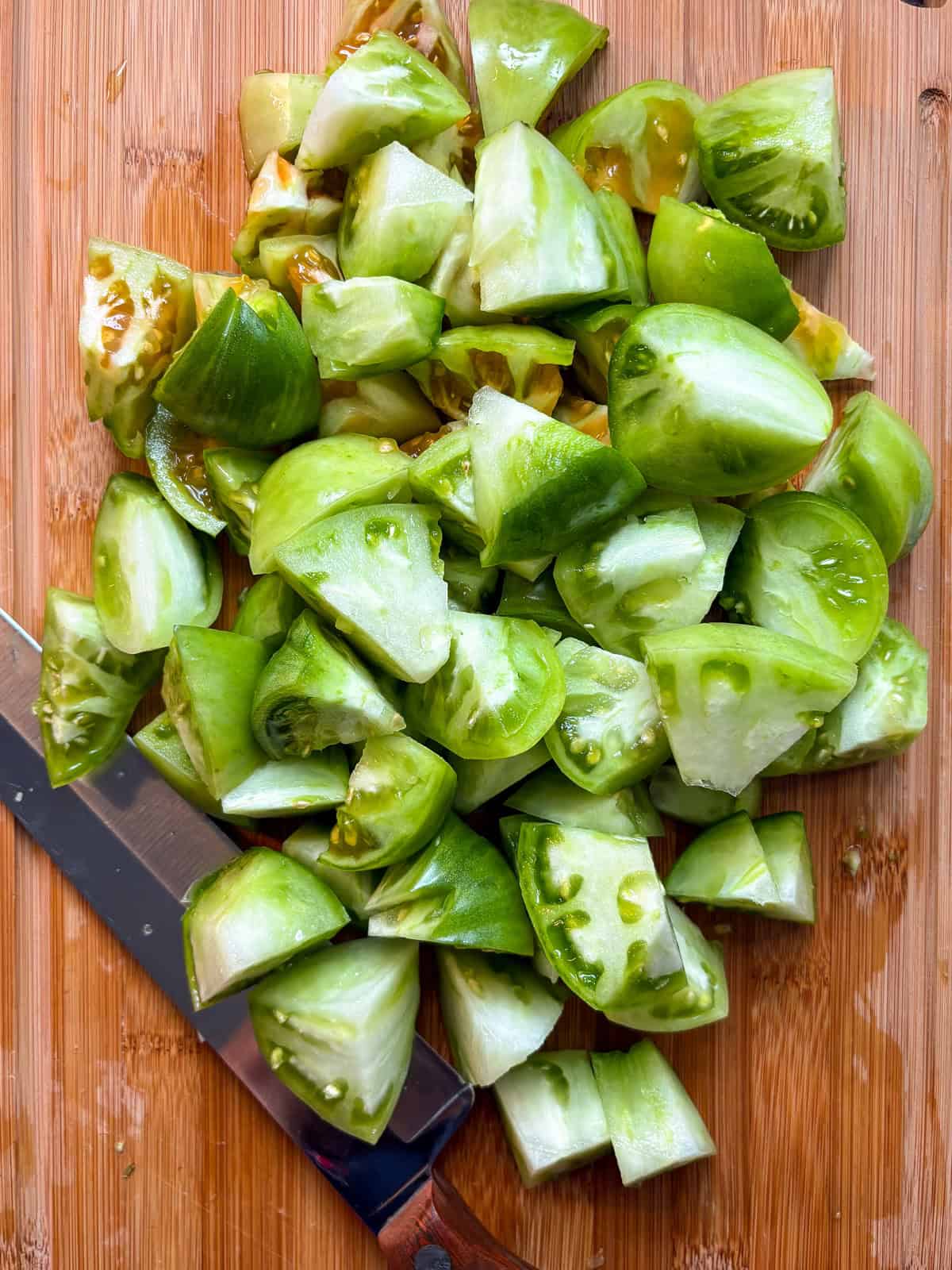 Green tomatoes, chopped, on a cutting board.