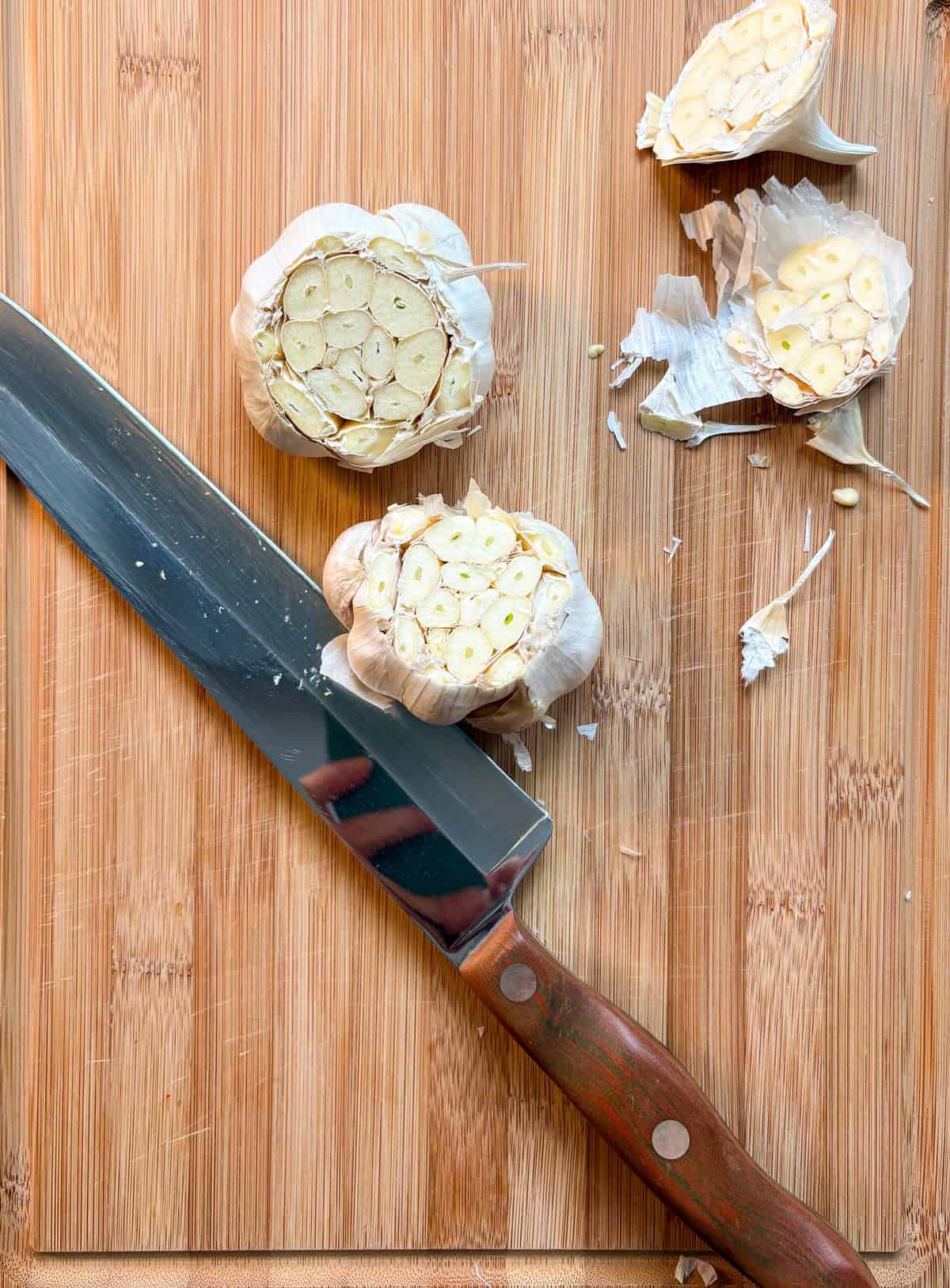 Two heads of garlic with the tops sliced off to reveal the cloves.
