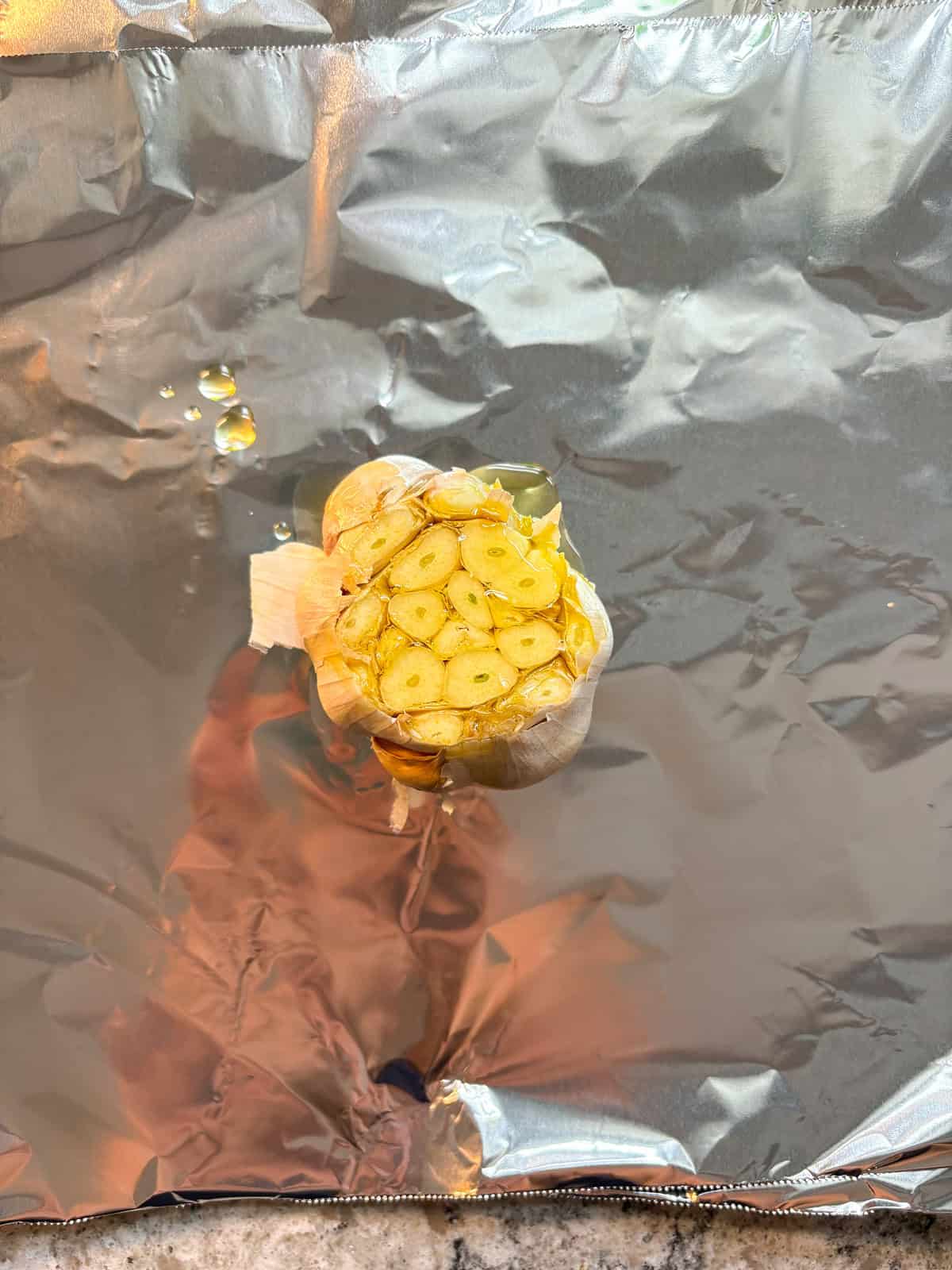 Oil drizzled over the head of garlic, on a sheet of foil.