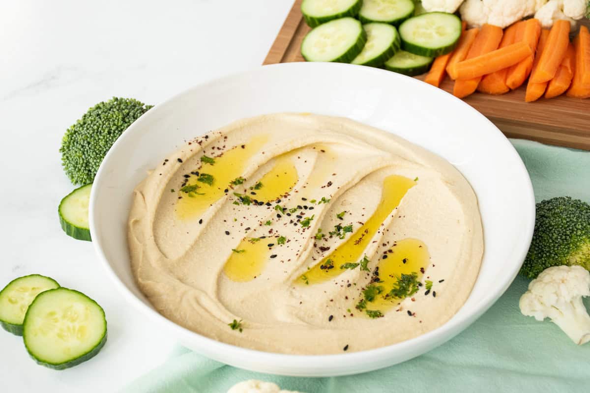 Bowl of creamy hummus, garnished with an olive oil drizzle, and a sprinkle of parsley, black sesame seeds, and sumac.
