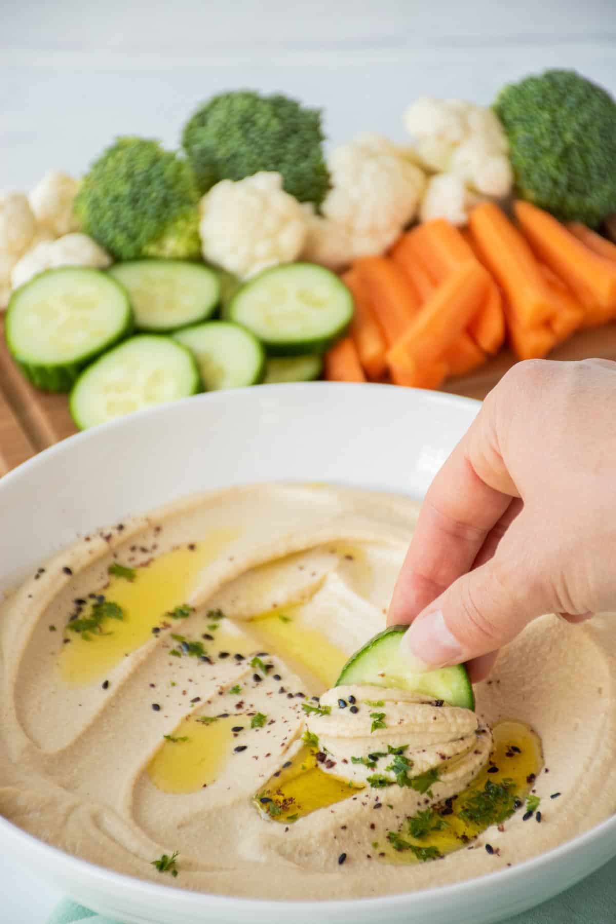 Cucumber slice being dipped into a bowl of hummus.