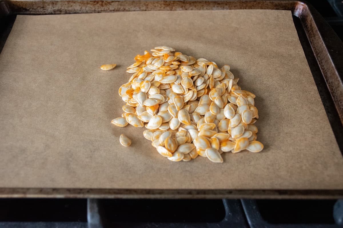 Raw pumpkin seeds on a lined baking sheet.