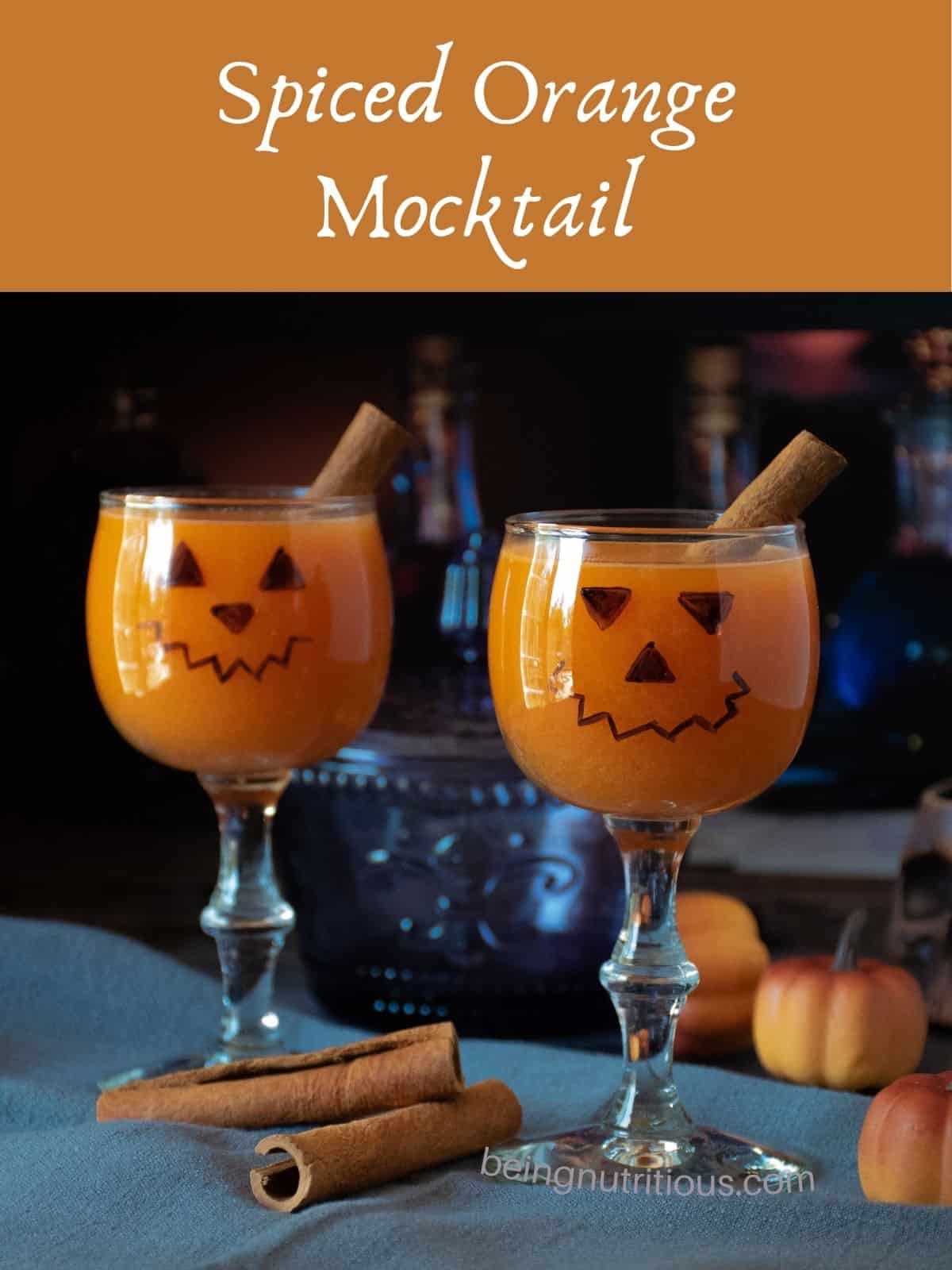 Two small wine glasses with jack-o-lantern face on them, with an orange beverage inside. Text overlay: Spiced Orange Mocktail.