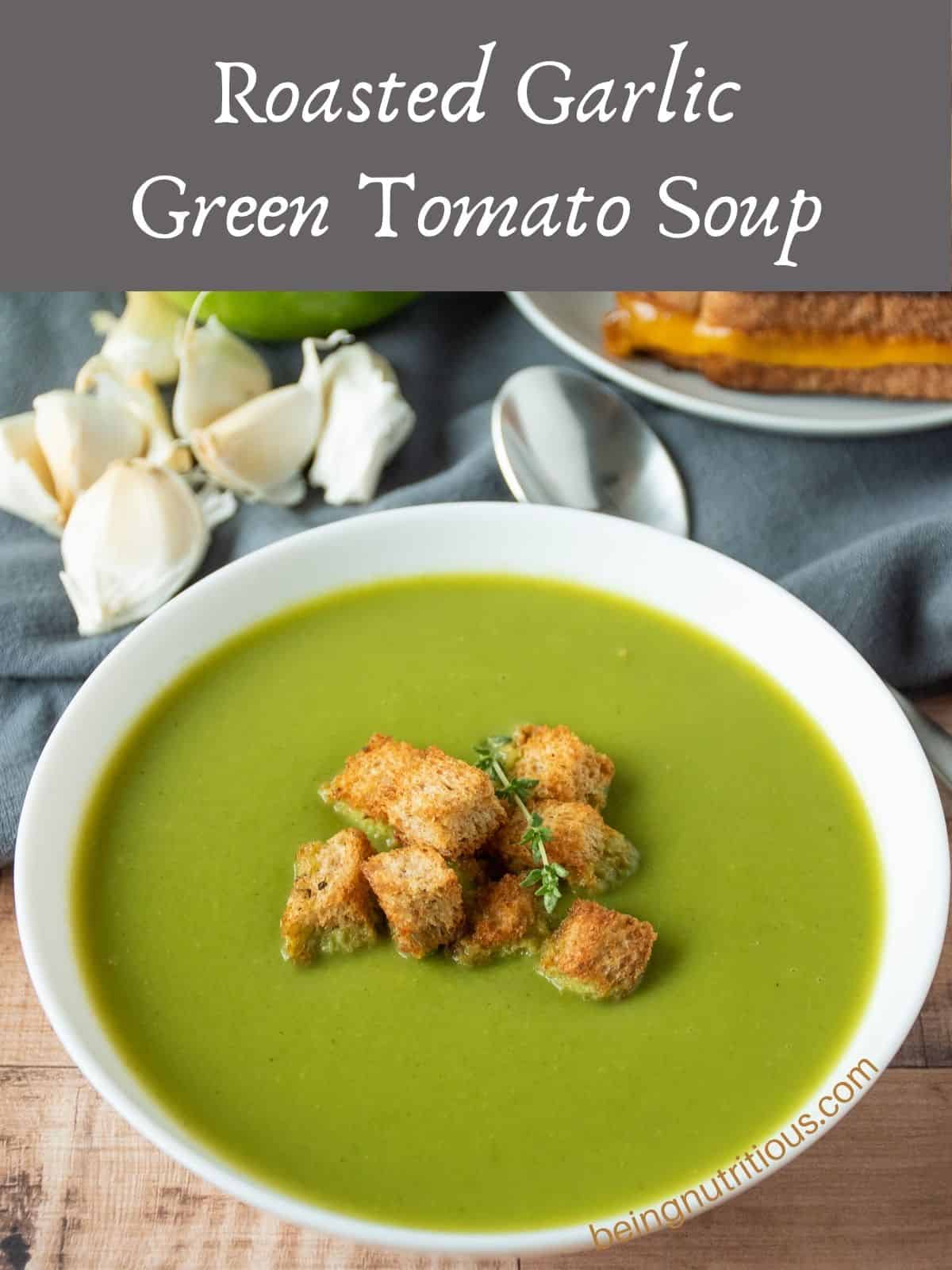 Green soup in a bowl, garnished with homemade croutons and fresh thyme. Text overlay: Roasted Garlic Green Tomato Soup.