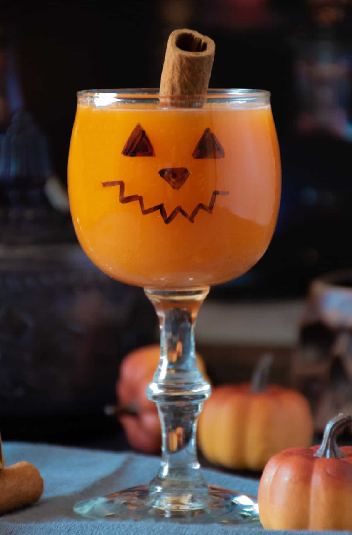 Small wine glass with a jack-o-lantern face on it, with an orange beverage inside.