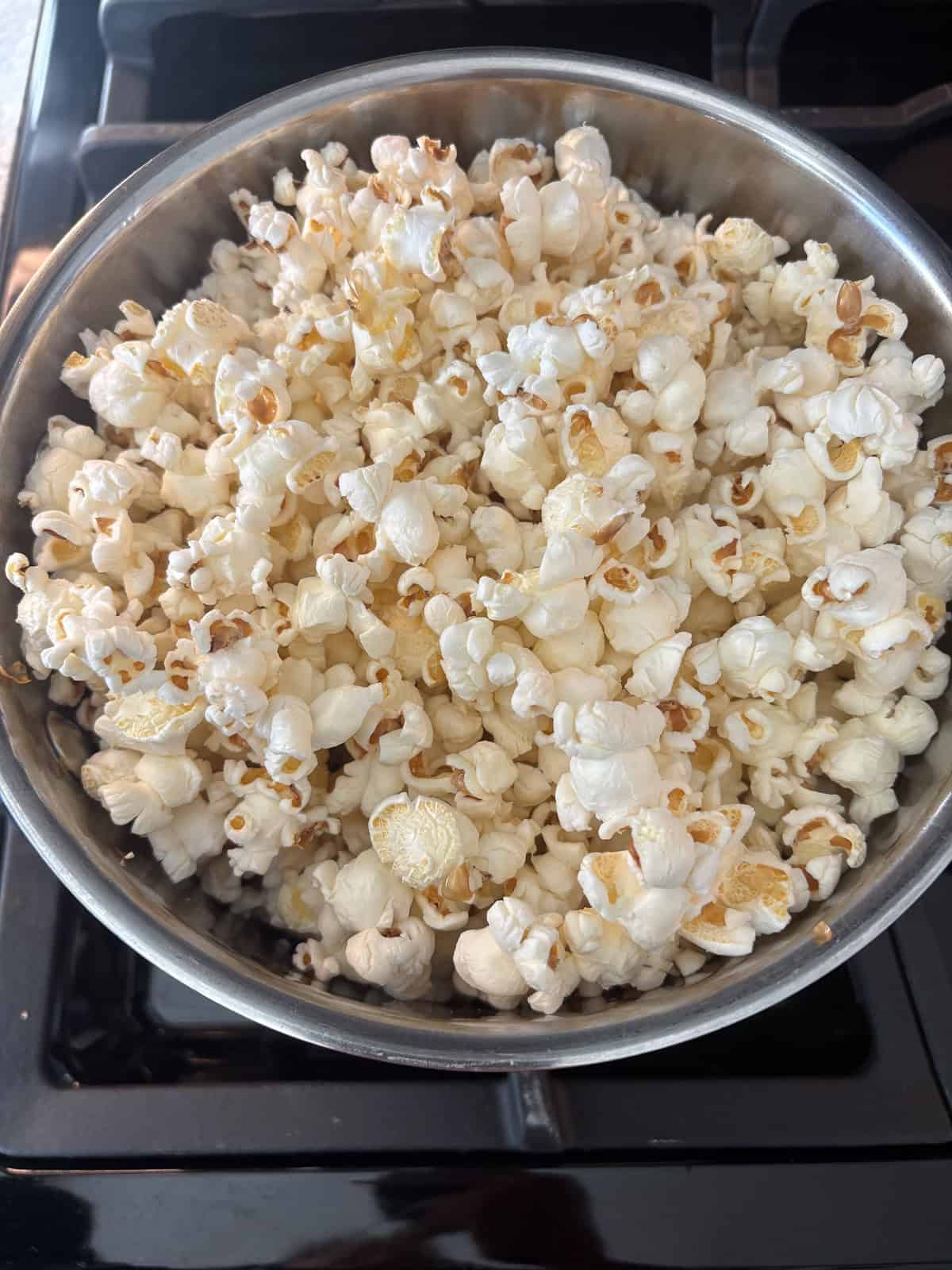 Pot on the stove, filled with popped popcorn.