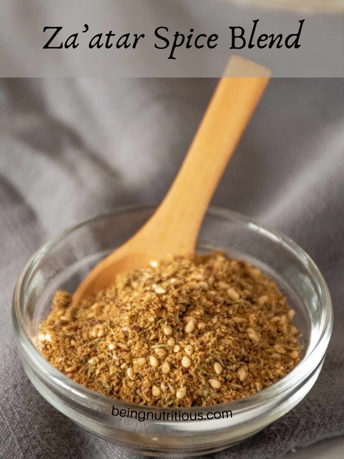 Small glass bowl with spice blend in it and a small wooden spoon. Text overlay: Za'atar Spice Blend.