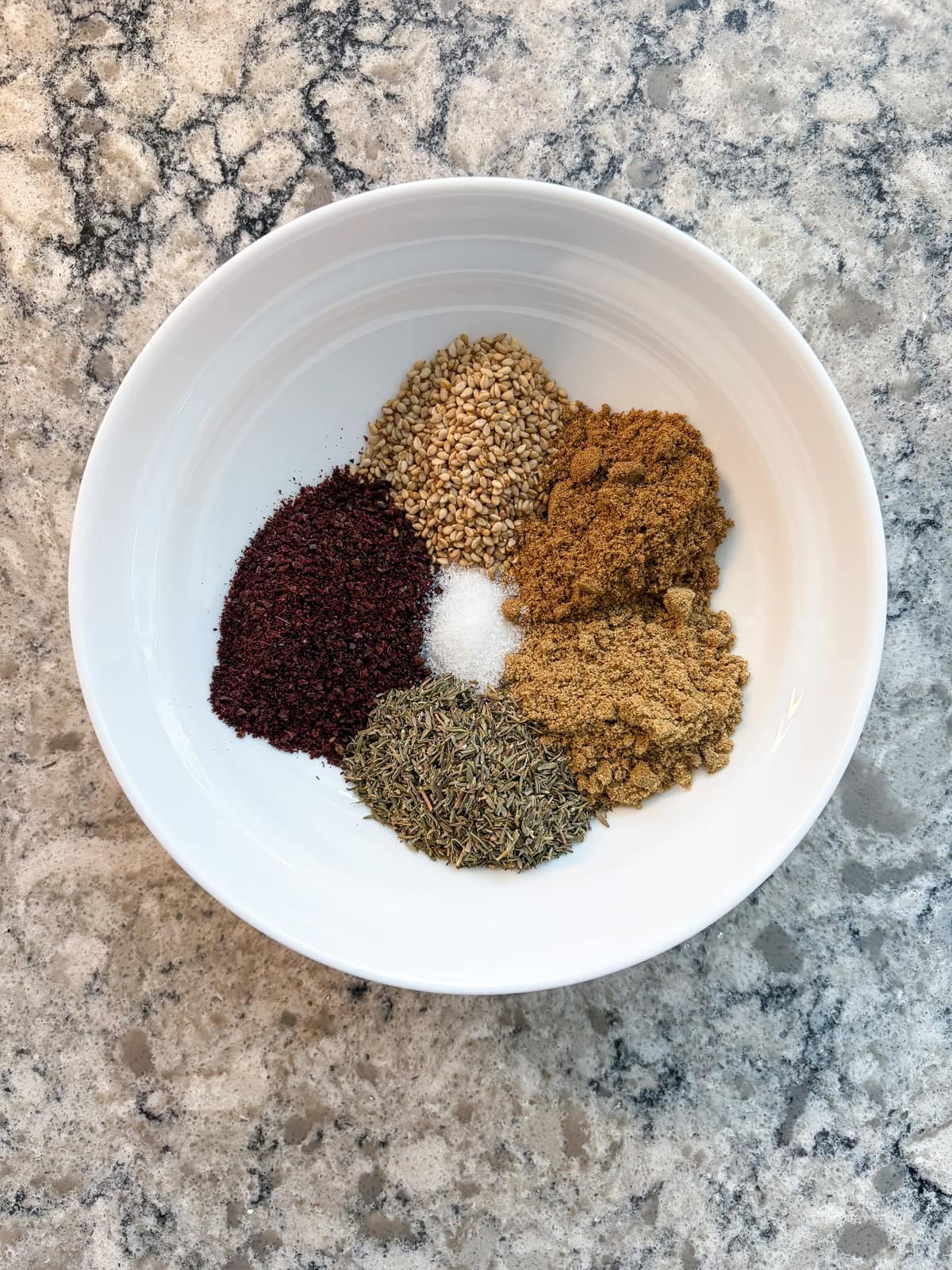 Small piles of 6 individual herbs and spices in a white bowl.