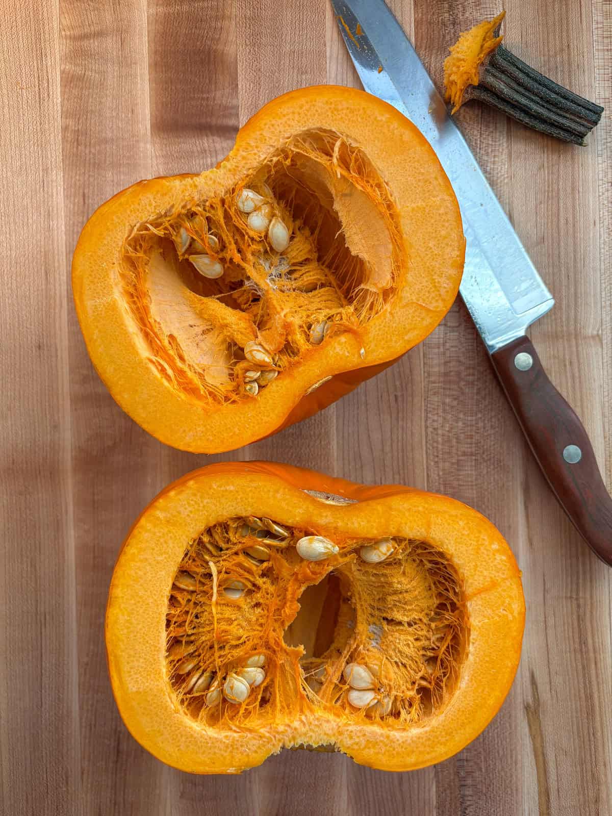Raw pumpkin, sliced in half, on a cutting board.