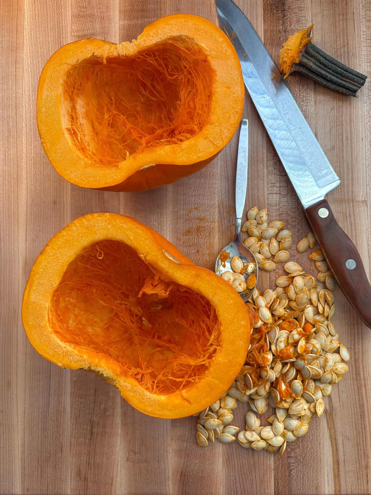 Raw pumpkin halves, face up on a cutting board, with the seeds removed.