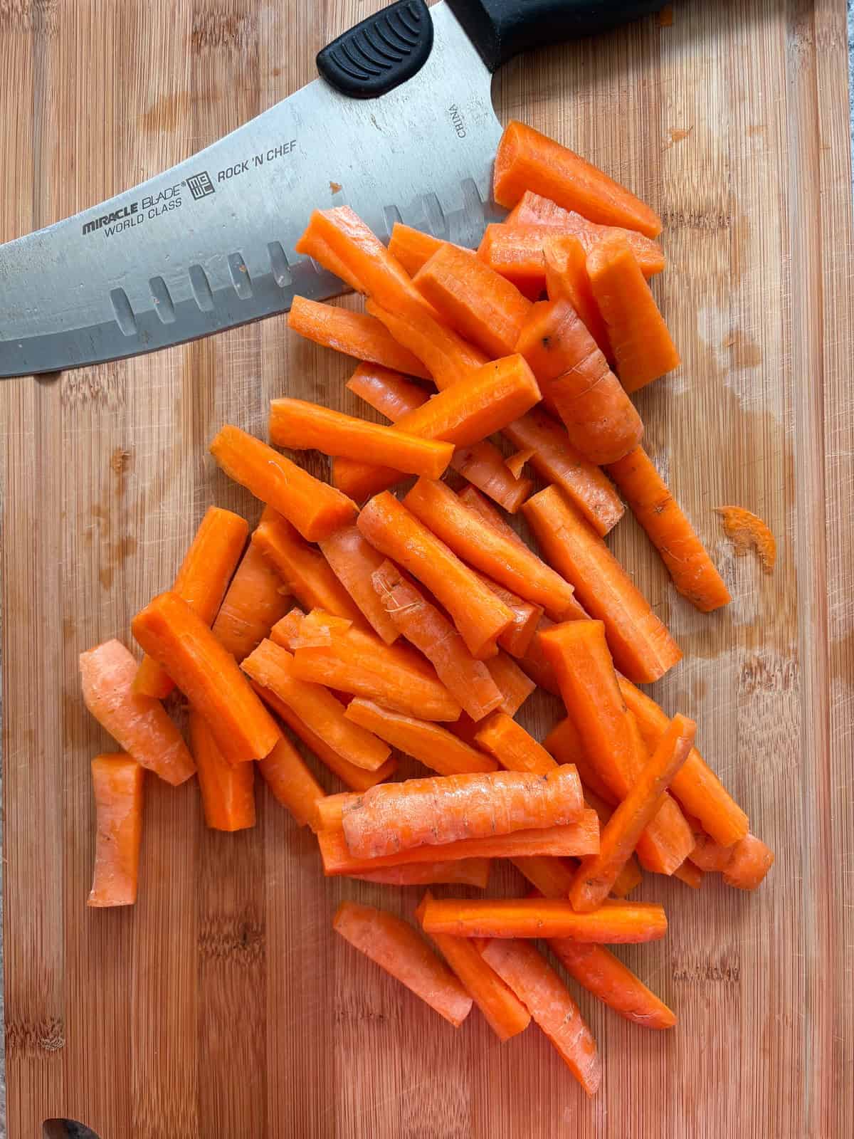 Carrots, cut into large matchsticks, on a cutting board.