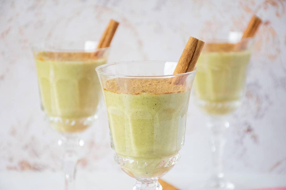 Three dessert glasses with green colored pudding in them, garnished with powdered cinnamon and a cinnamon stick.