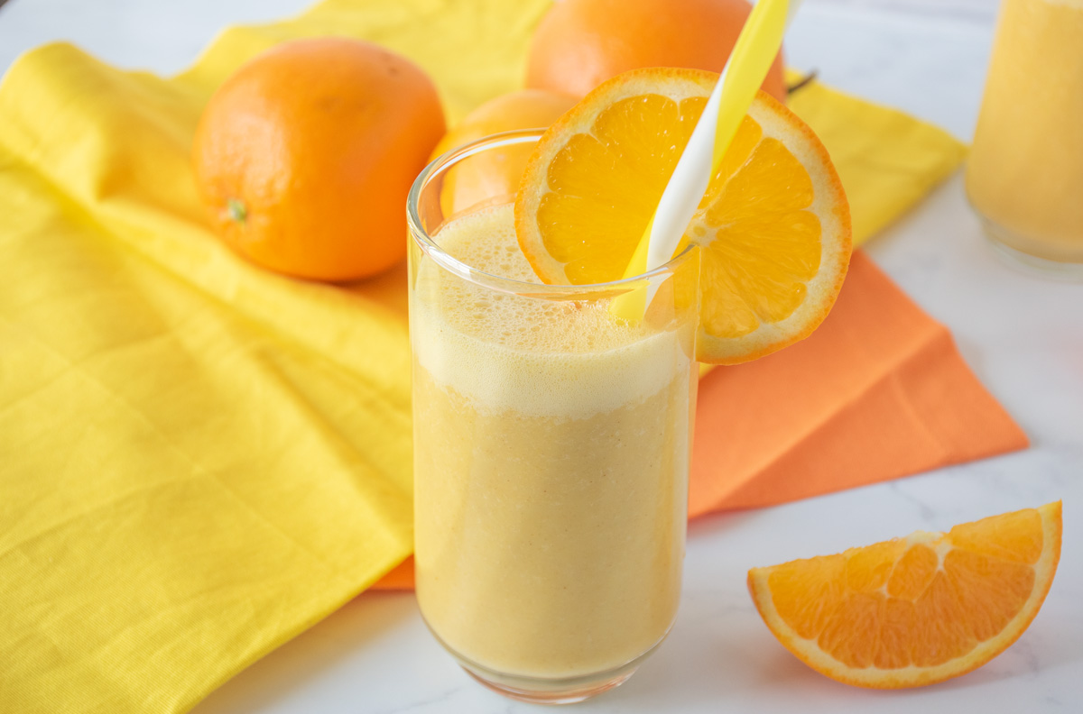 Orange drink in a glass with a straw, garnished with an orange slice.