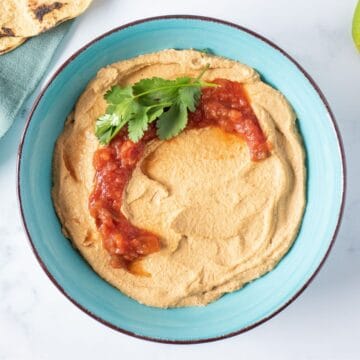 Bowl of hummus, garnished with salsa and cilantro.