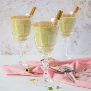 Three dessert glasses with green colored pudding in them, garnished with powdered cinnamon and a cinnamon stick.