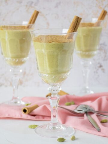 Three dessert glasses with green colored pudding in them, garnished with powdered cinnamon and a cinnamon stick.