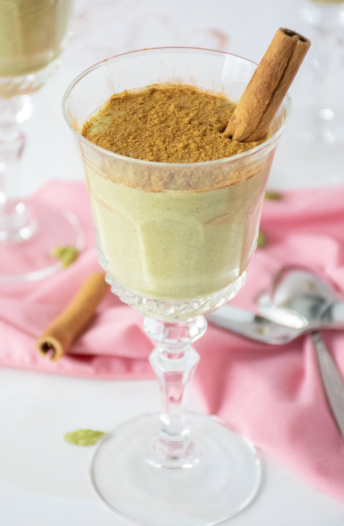 A stemmed dessert glass with green colored pudding in it, garnished with powdered cinnamon and a cinnamon stick.