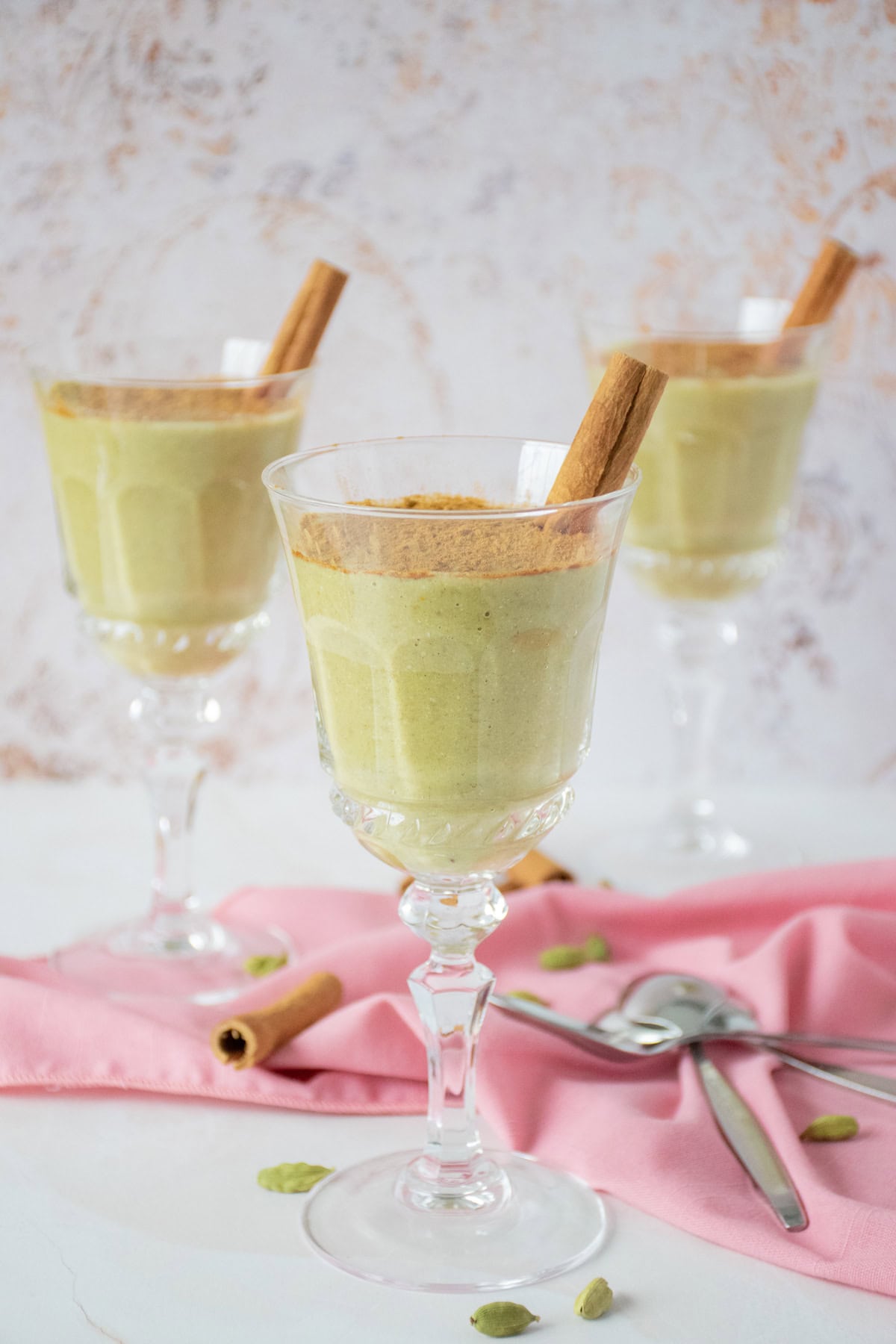 Three dessert glasses with green colored pudding in them, garnished with powdered cinnamon and a cinnamon stick.