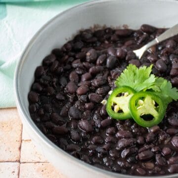 Bowl of black beans garnished with cilantro and jalapeno slices.