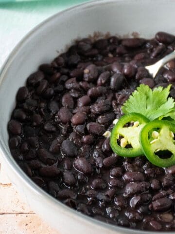 Bowl of black beans garnished with cilantro and jalapeno slices.