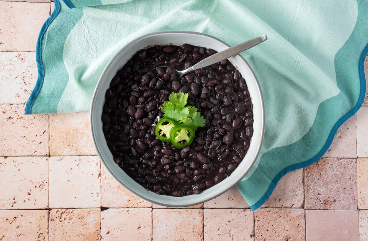 Bowl of black beans garnished with cilantro and jalapeno slices.
