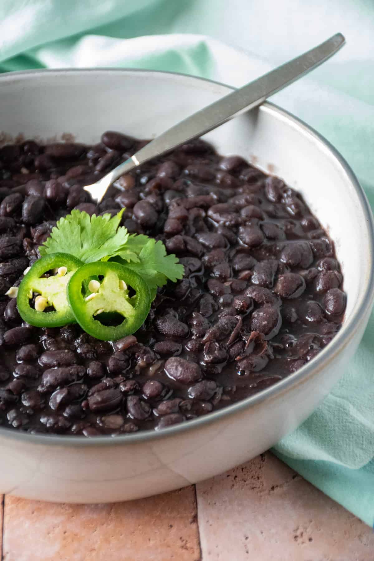 Bowl of black beans garnished with cilantro and jalapeno slices.
