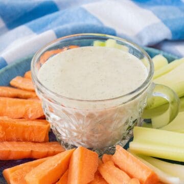 Small plate with carrot and celery sticks on it, and a small bowl of ranch dressing in the middle.