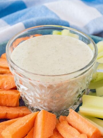 Small plate with carrot and celery sticks on it, and a small bowl of ranch dressing in the middle.