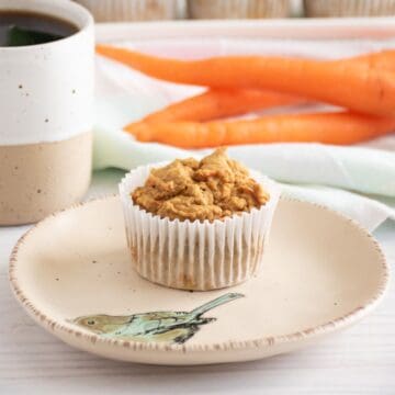 A muffin on a plate, with a cup of coffee nearby.