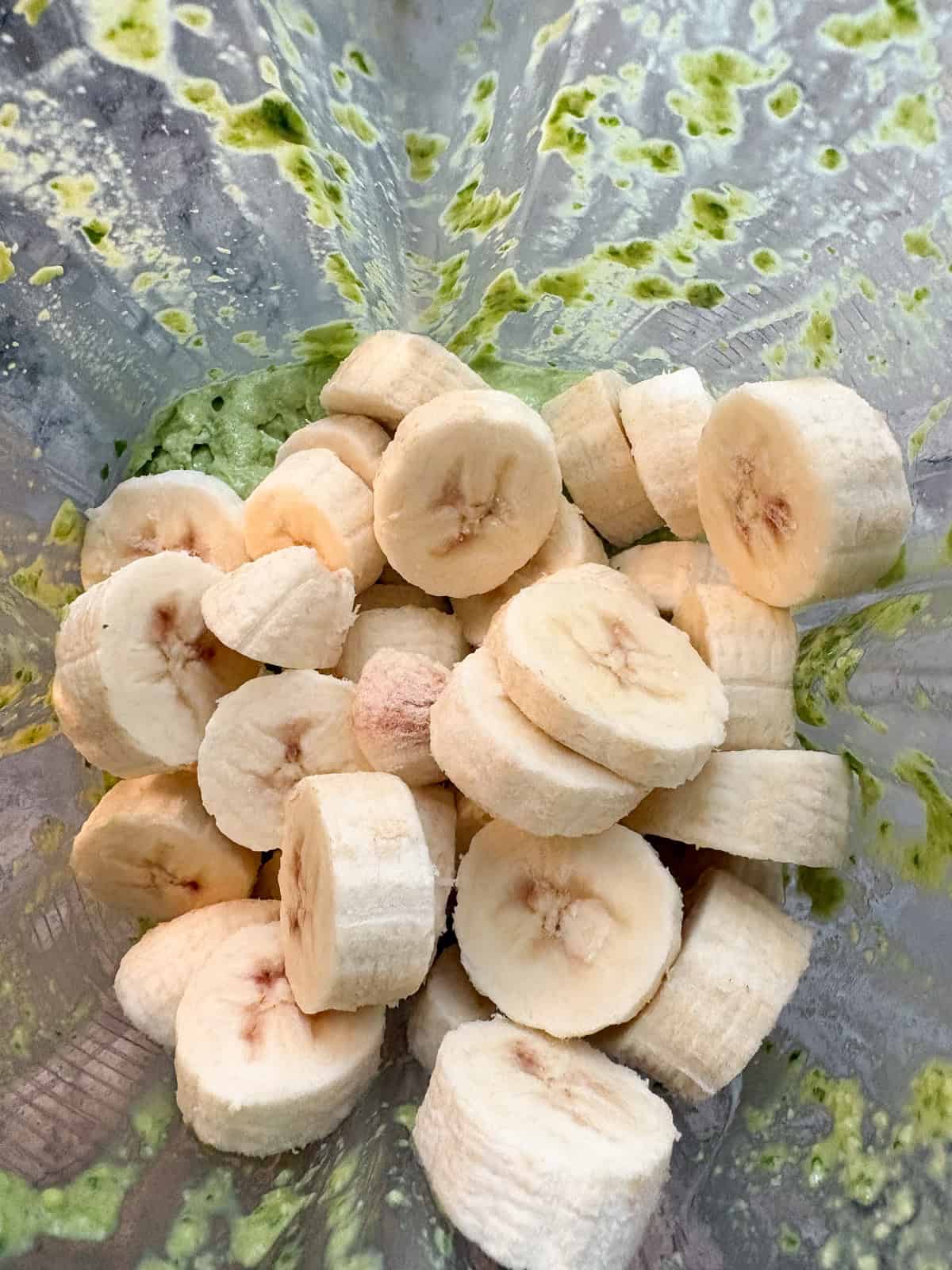 Frozen banana slices added to the avocado spinach mixture in a blender.