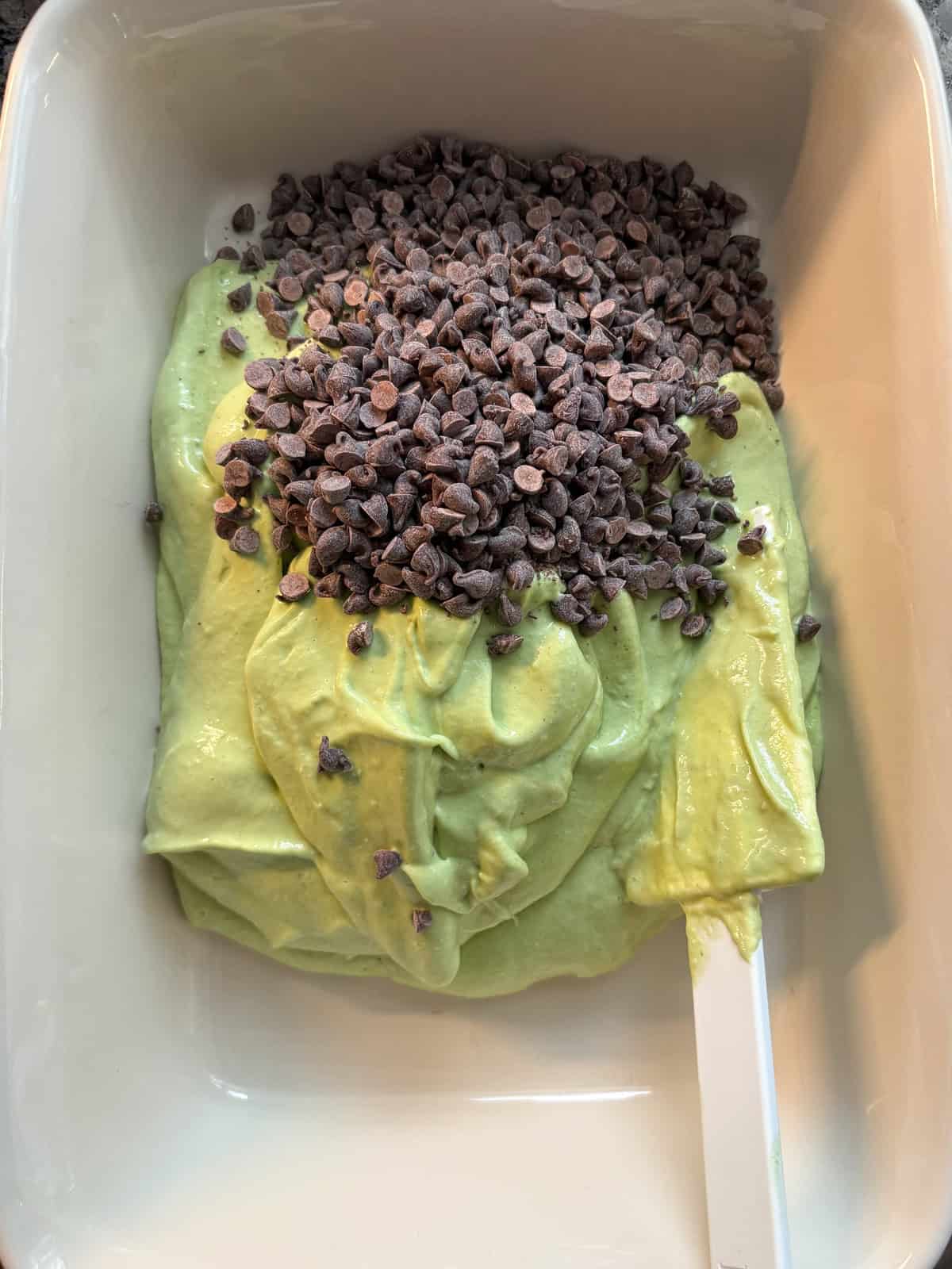 Mint ice cream in a pan, with chocolate chips poured on top.