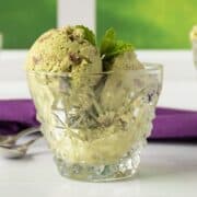 Small glass mug of green colored ice cream with chocolate chips, garnished with fresh mint leaves.