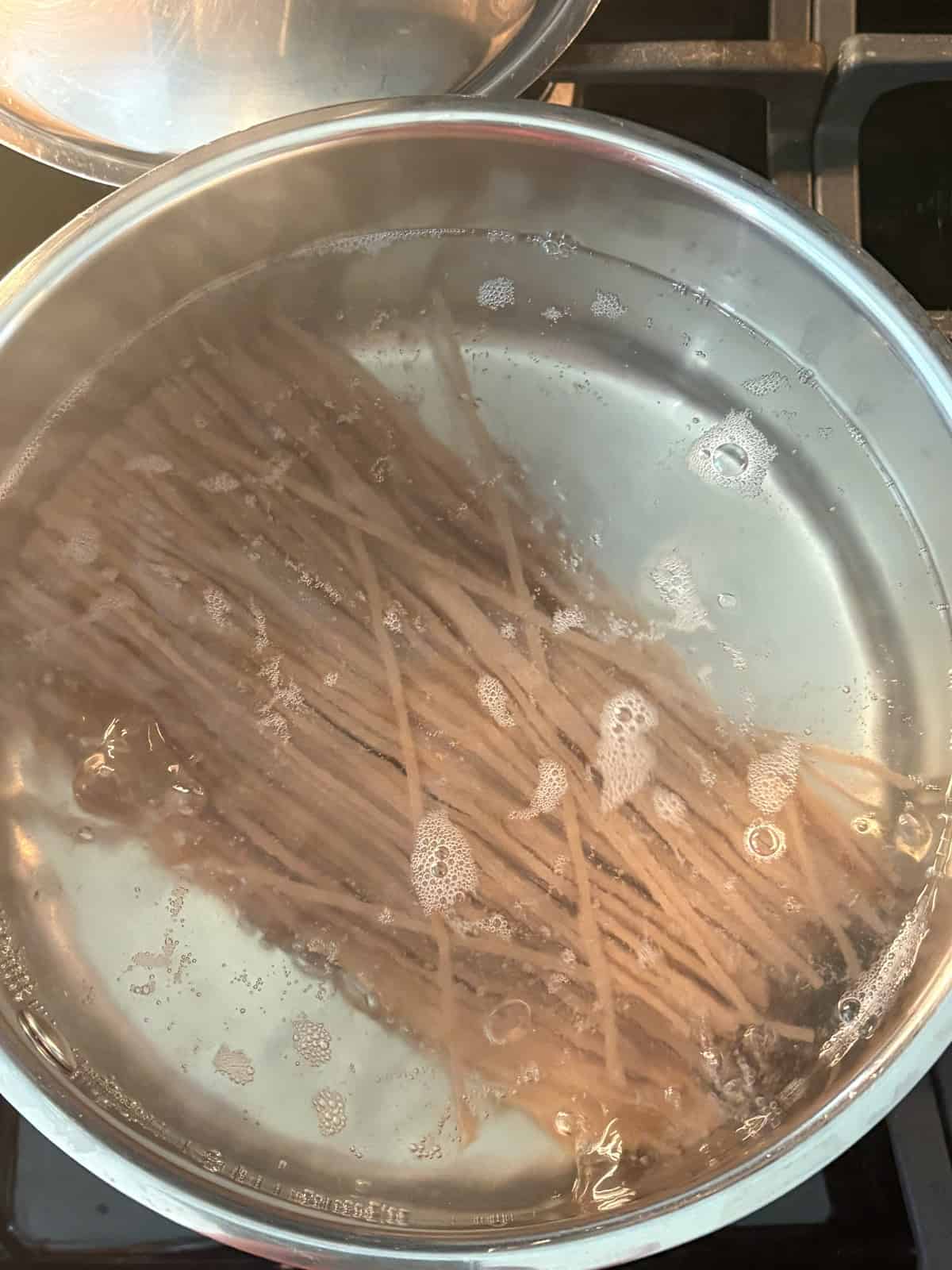 Dry soba noodles added to a pot of boiling water.