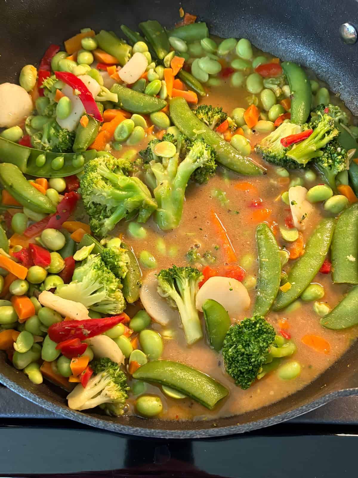 Sauce poured over sauteed vegetables in a skillet.