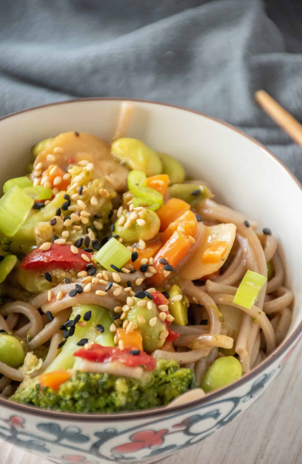 Close up of a bowl of noodles and vegetables, garnished with black and white sesame seeds, and chopped green onions.