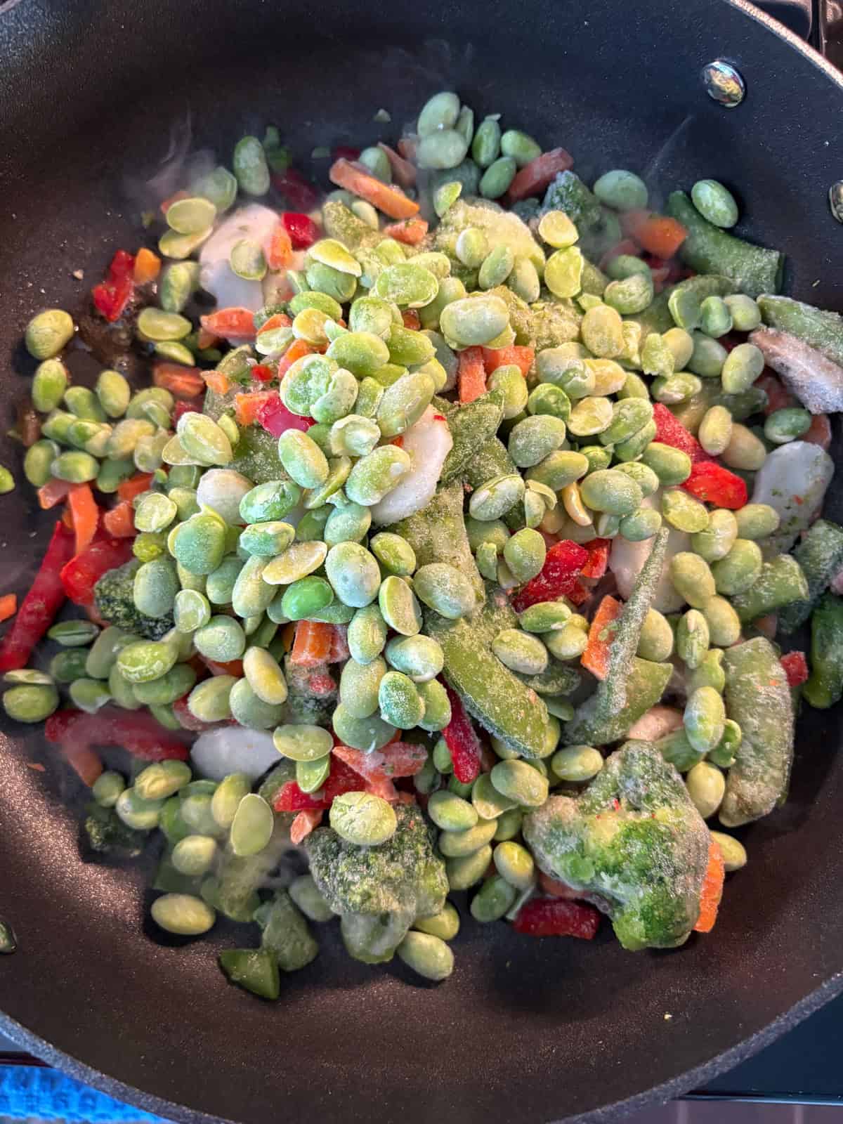 Frozen stir fry vegetables and edamame added to a hot skillet.