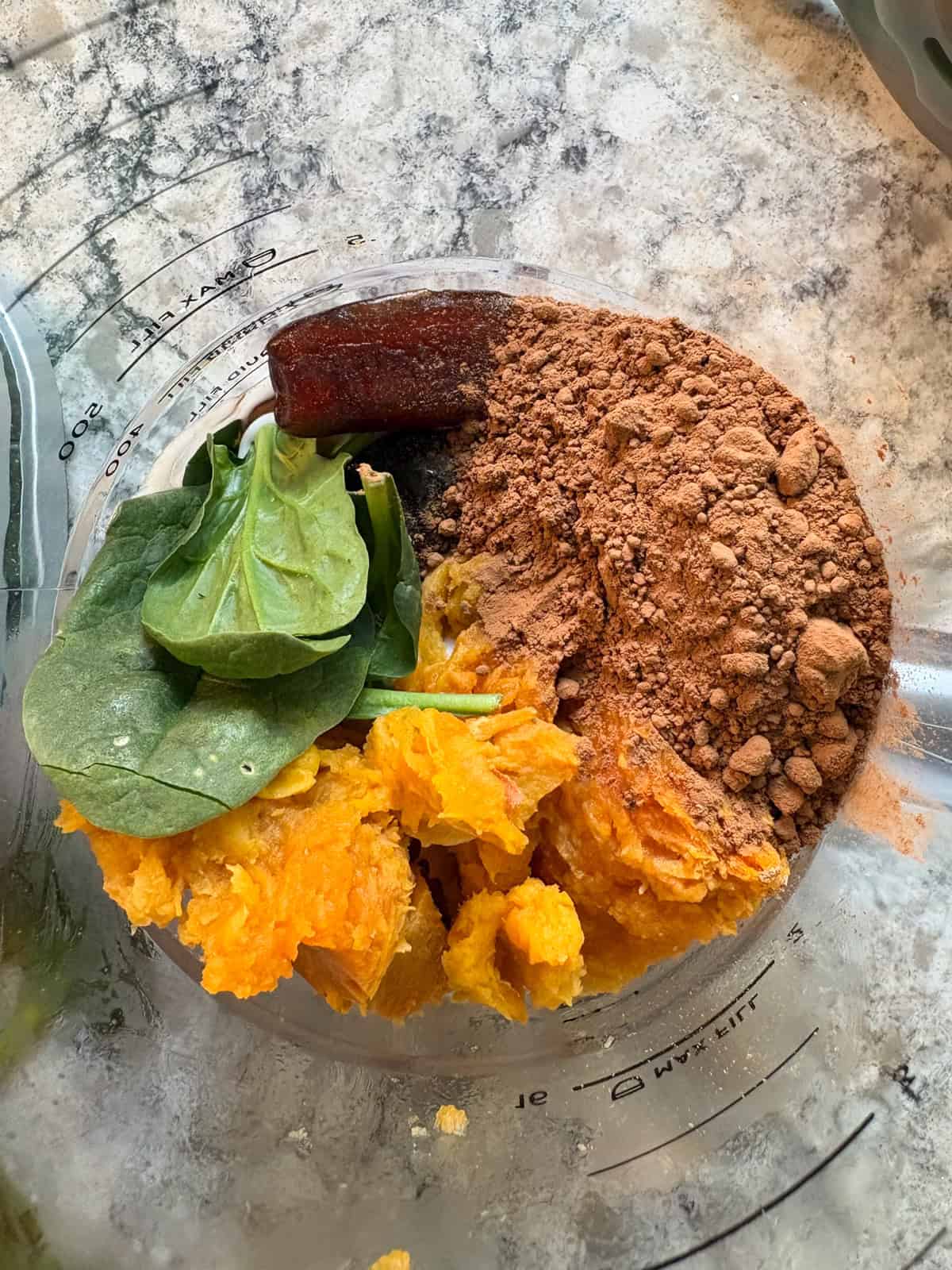 Yogurt, dates, sweet potato, cocoa powder, and spinach added to a blender.