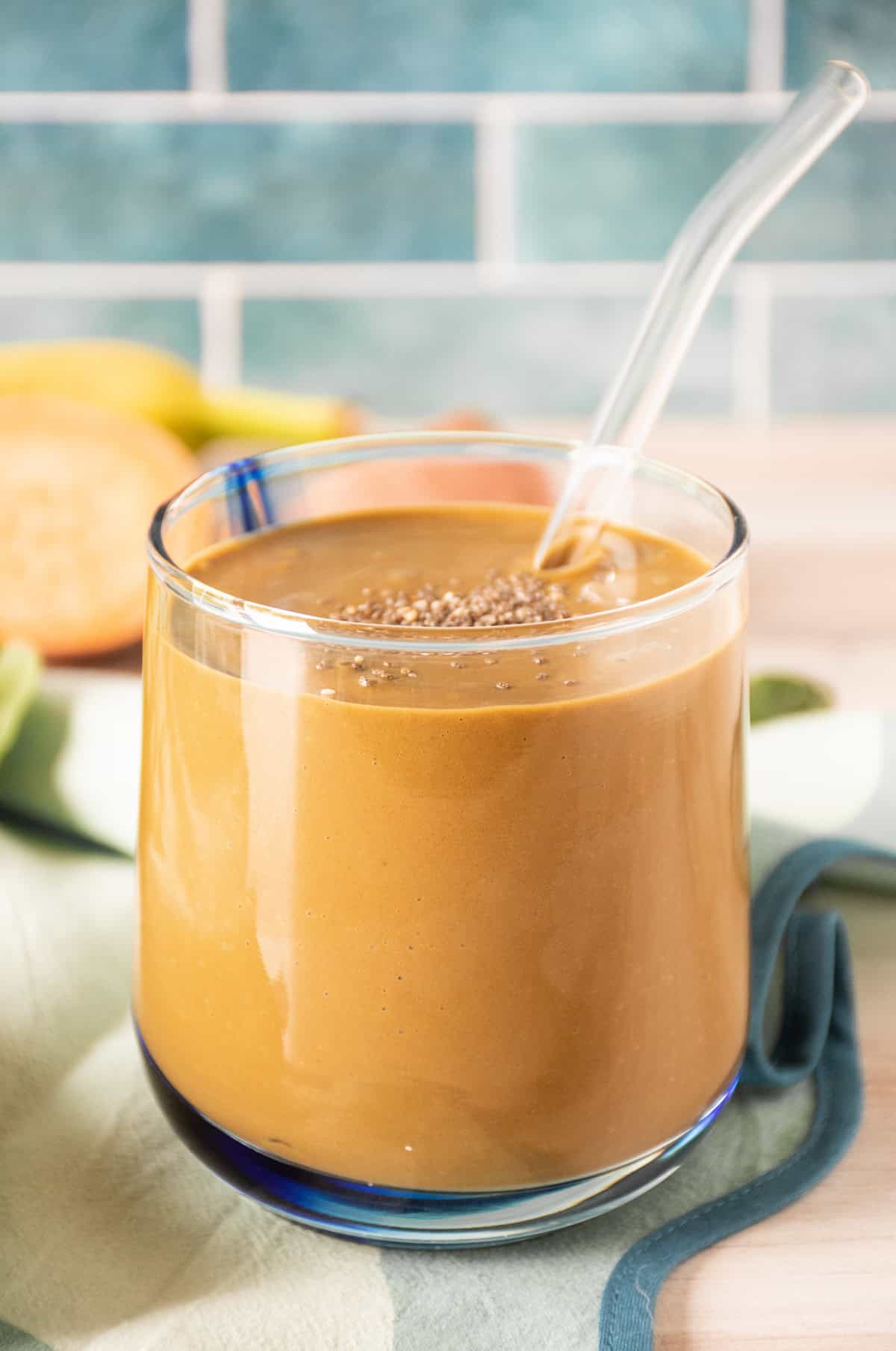 Chocolate smoothie in a glass, with a clear straw, sprinkled with chia seeds.