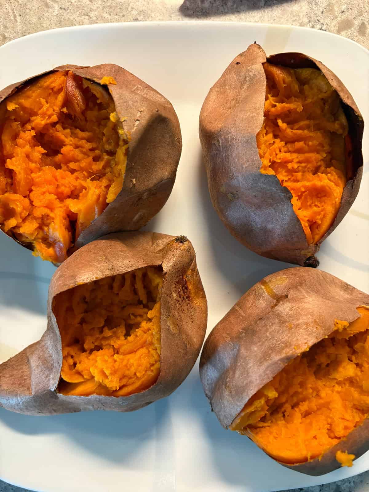 Four baked sweet potatoes on a plate, cut open and slightly mashed.