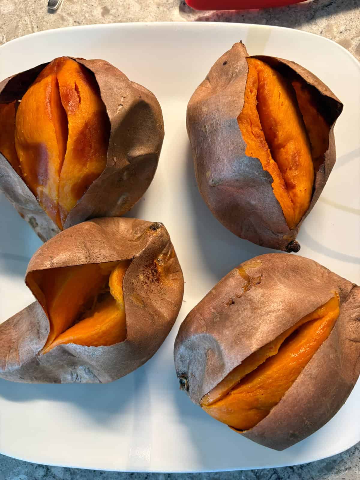 Four sweet potatoes on a dish, cut and smushed open.