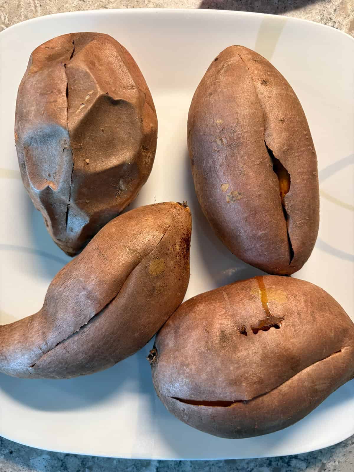 Four baked sweet potatoes on a plate, cut open