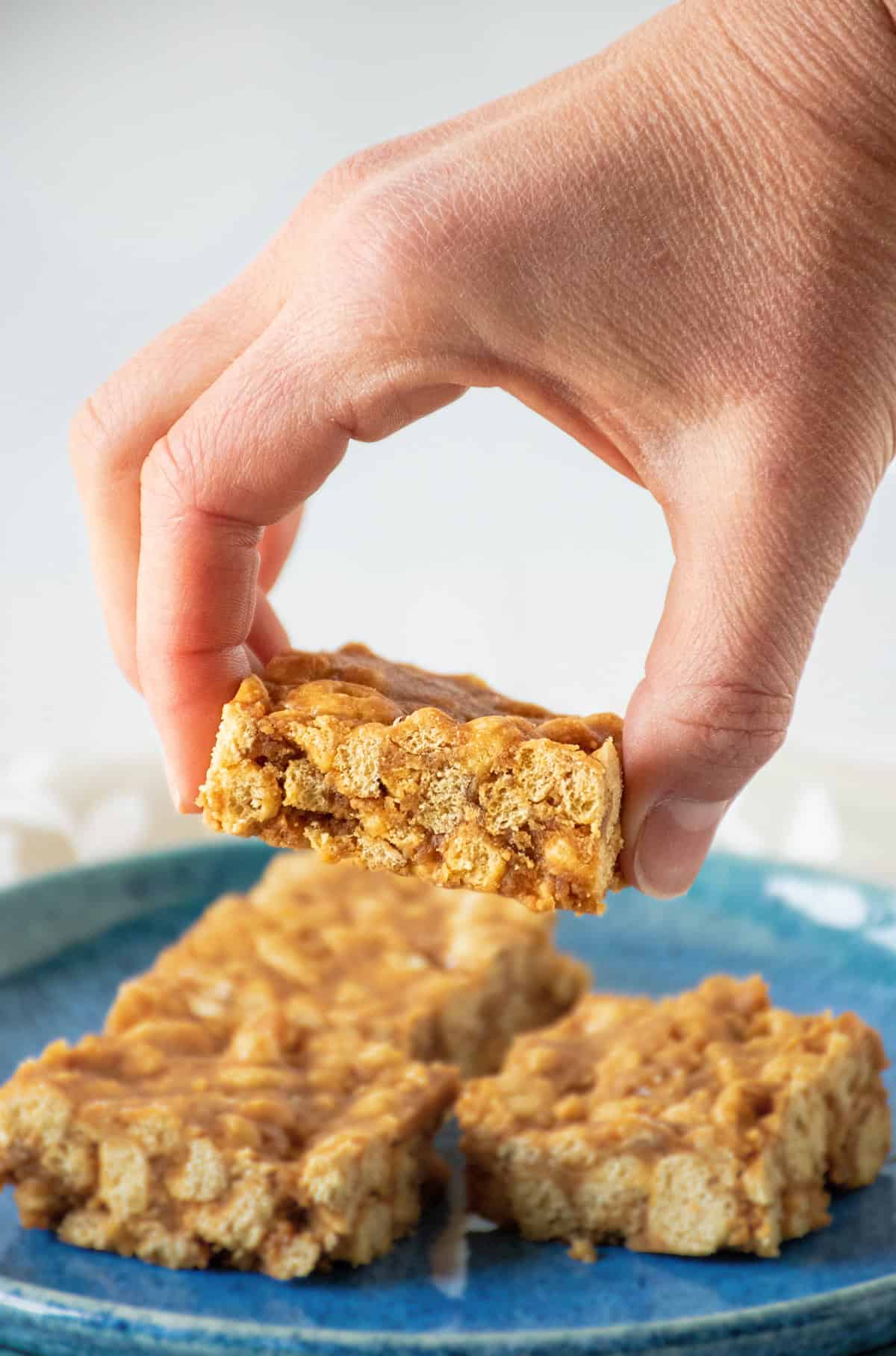 A hand lifting a cereal bar off a serving dish.
