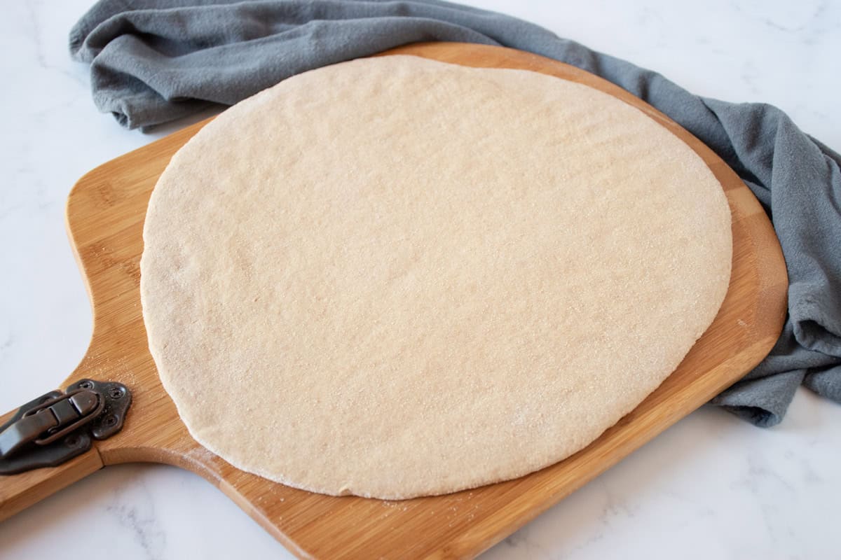 Raw pizza dough, rolled out to a circle, on a pizza peel.