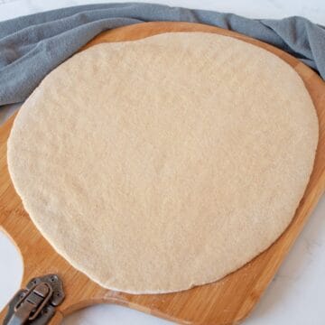 Raw pizza dough, rolled out to a circle, on a pizza peel.