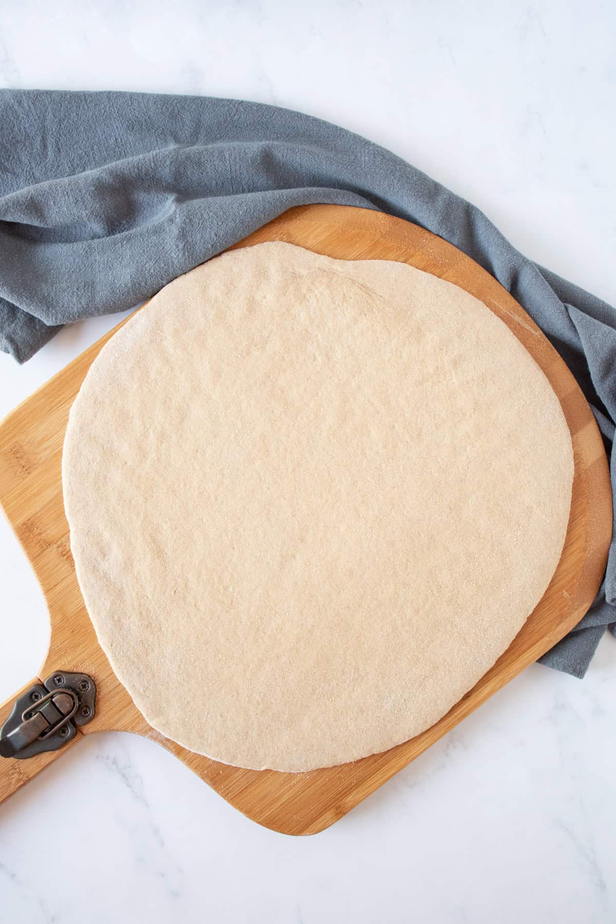 Raw pizza dough, rolled out to a circle, on a pizza peel.