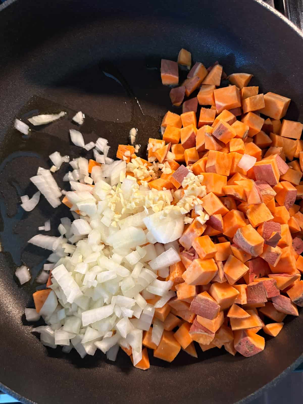 Chopped sweet potatoes, onions, and garlic, sauteing in a pan.